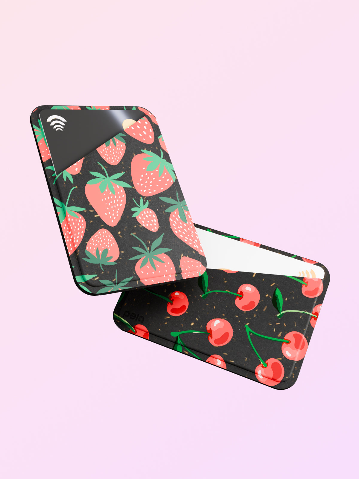 Two Pela Mini Wallets are displayed against a light pink background. One wallet features a vibrant strawberry pattern with green leaves on a dark background, while the other showcases a cherry design with red cherries and green stems. Both wallets have a sleek, modern look with a small card slot visible.