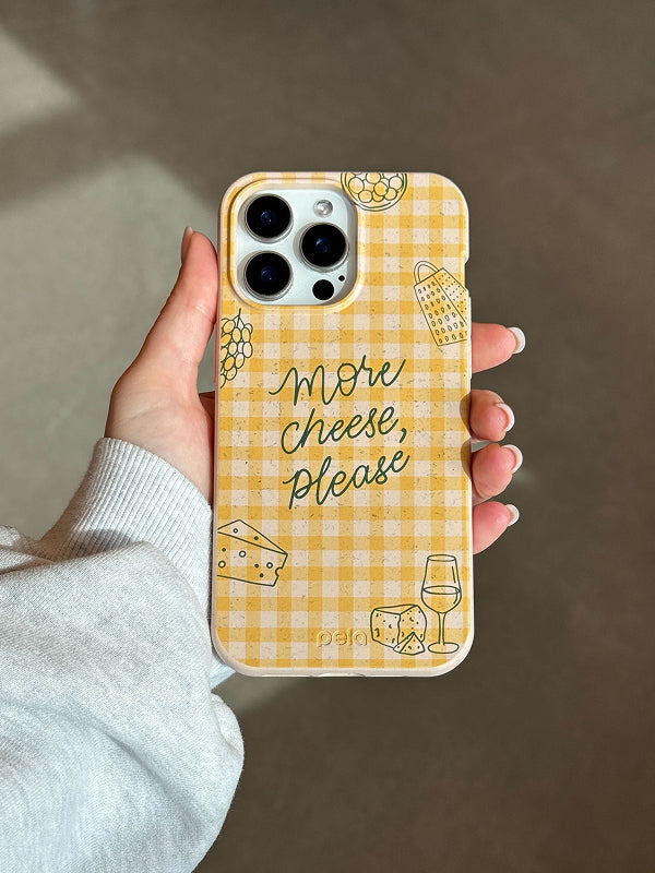 A hand holding the Pela More Cheese Phone Case featuring a yellow gingham background with cheese, grapes, and wine glass illustrations.